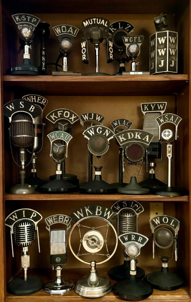 A collection of vintage microphones with radio station call letter flags. Stations include: WIP, Philadelphia; WEBR, Buffalo; WKBW, Buffalo, WRR, Dallas